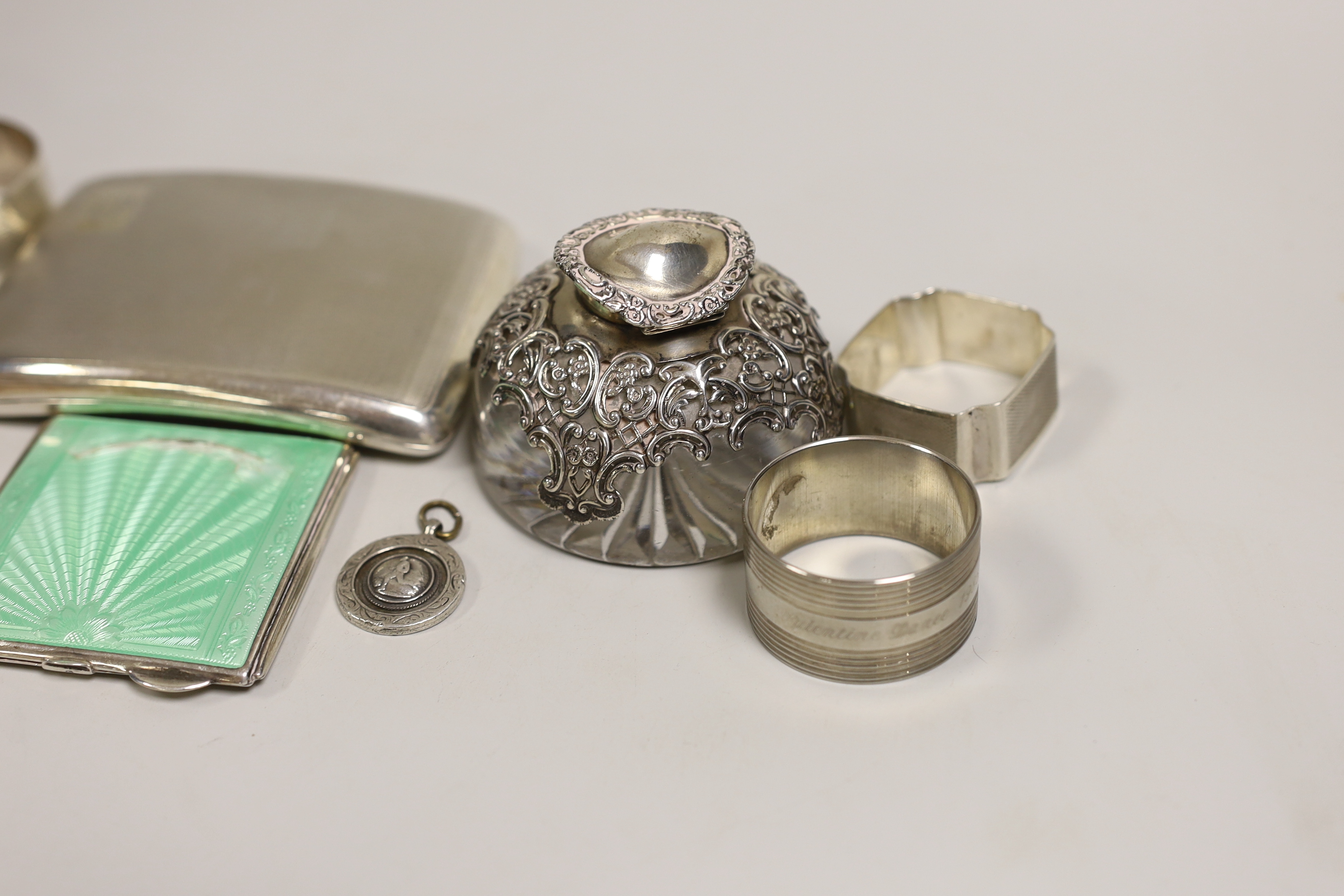 A quantity of mixed silver ware including a cigarette case and enamelled compact (a.f.), a mounted glass inkwell, five napkin rings, (one plated), a brooch and a Fattorini & Sons football pendant.